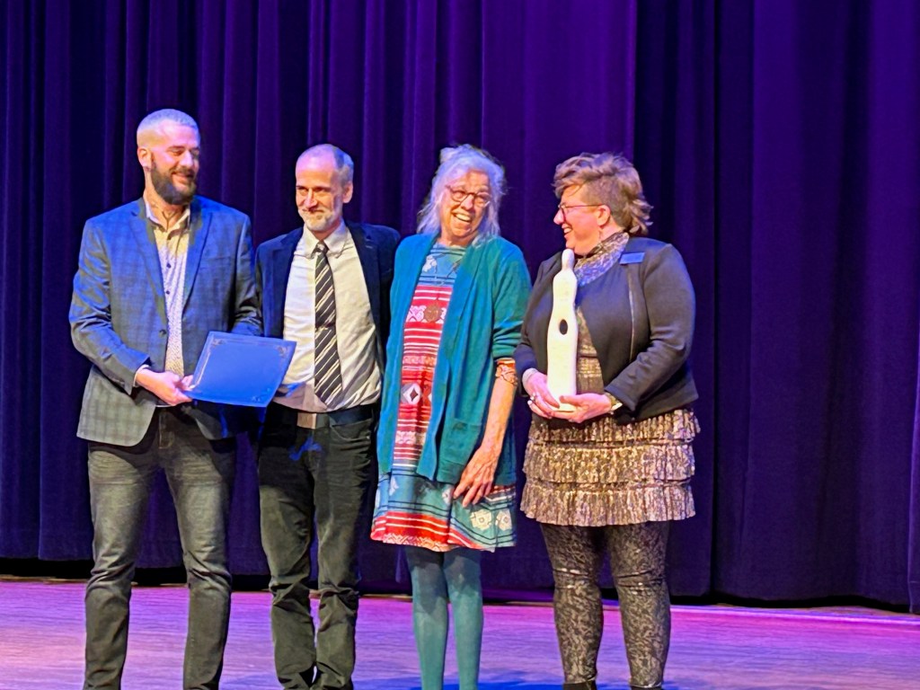 Casey Grooten presents the certificate to Scott Bade and Elizabeth Kerlikowske. Kim Shaw holds the sculpture 'Enigma' created by William Glass.