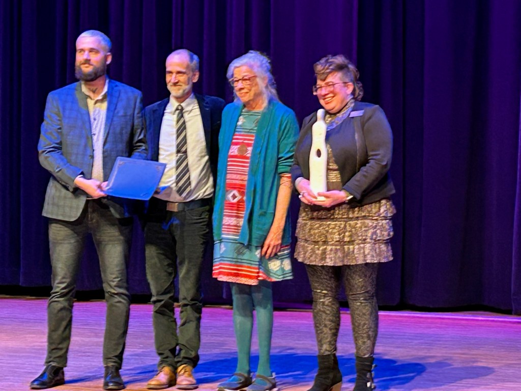 Casey Grooten presents the certificate to Scott Bade and Elizabeth Kerlikowske. Kim Shaw holds the sculpture 'Enigma' created by William Glass.