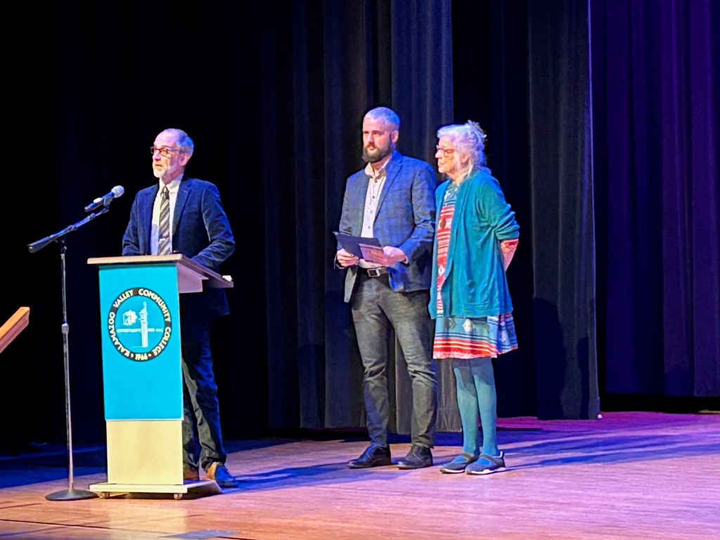 President Scott Bade offers words of thanks at a podium while Elizabeth Kerlikowski and Casey Grooten stand in the background.