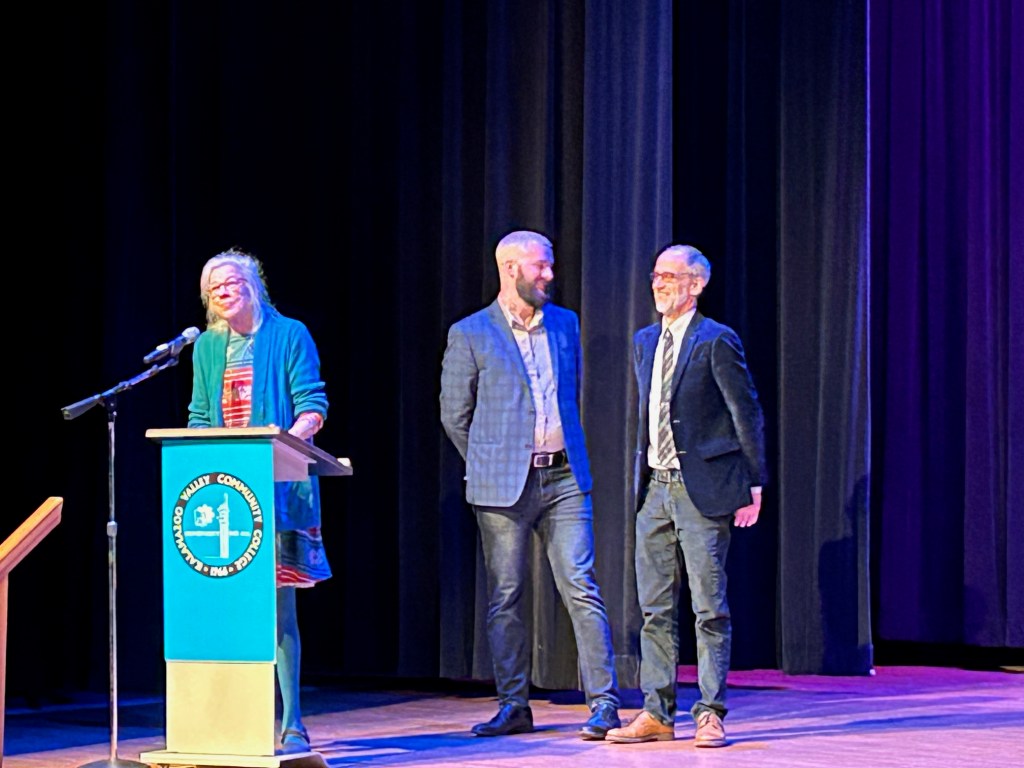 Former President Elizabeth Kerlikowski offers words of thanks at a podium while Scott Bade and Casey Grooten stand in the background.